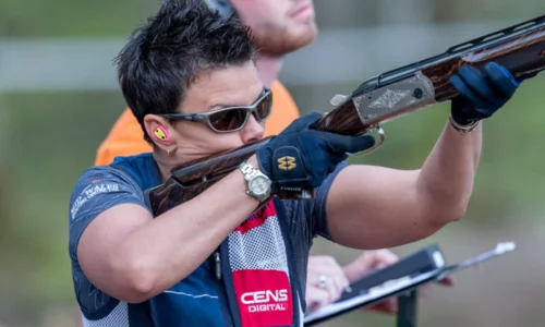 Woman holding a competitive shooting gun, wearing shooting ear plugs.